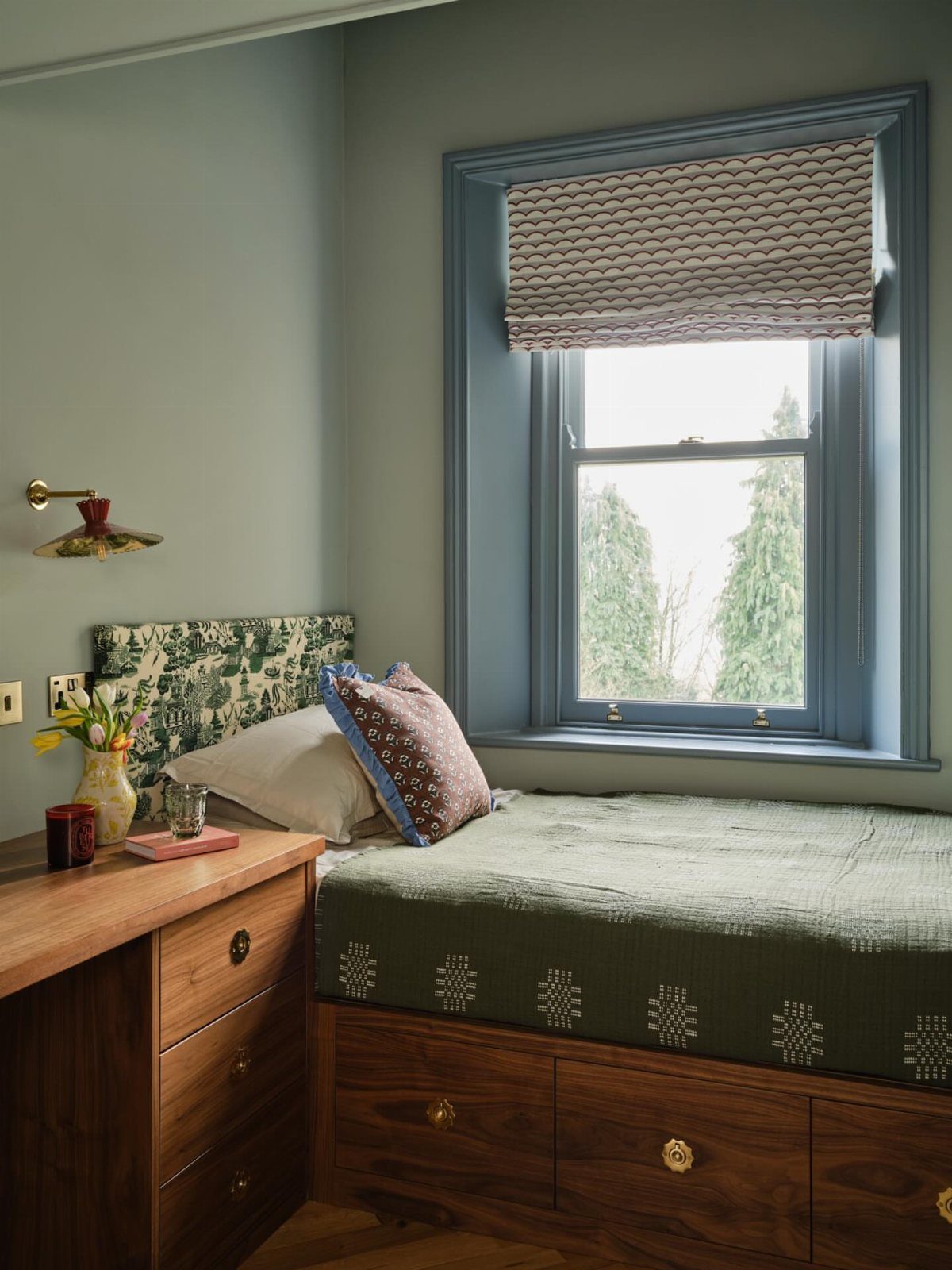 Bed with built-in wooden drawers under a green patterned mattress in a cozy nook.