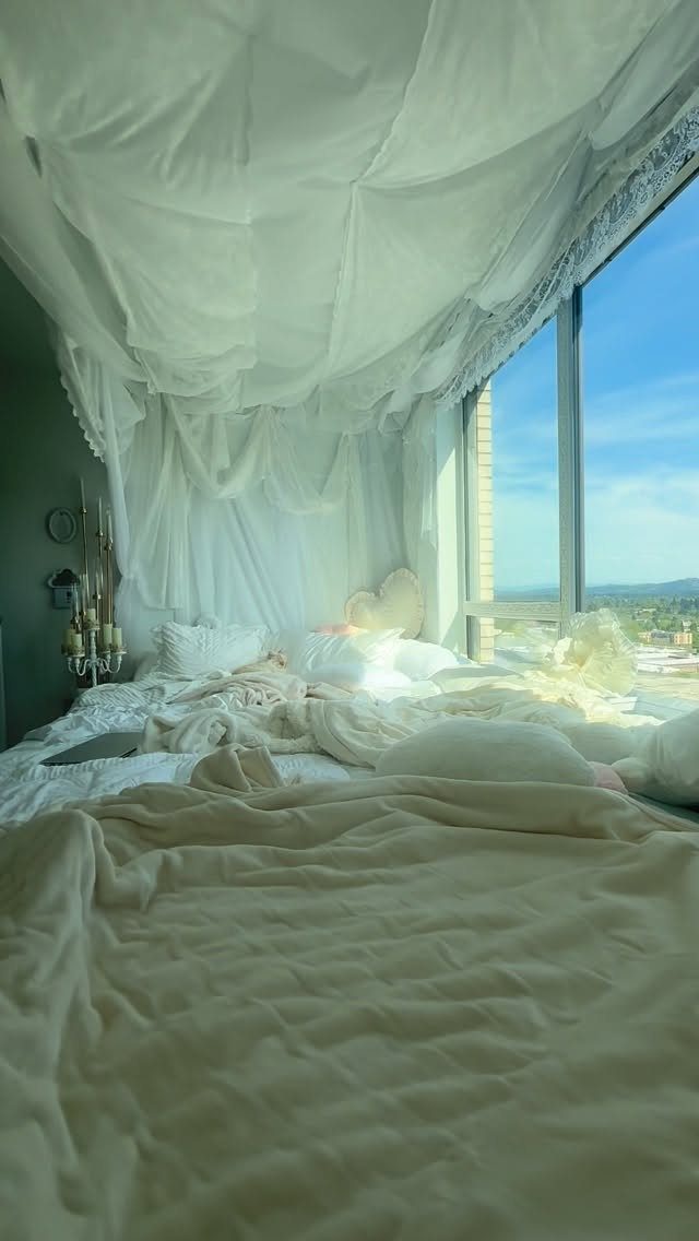 Bed with white linens and a flowing white fabric canopy draped from the ceiling.