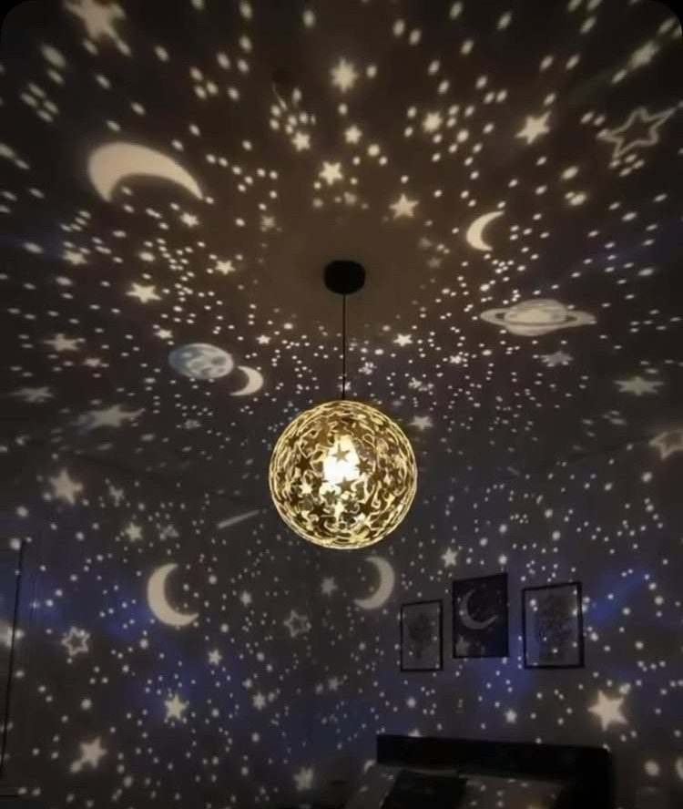 Spherical gold lamp projecting stars and moons onto a dark bedroom ceiling