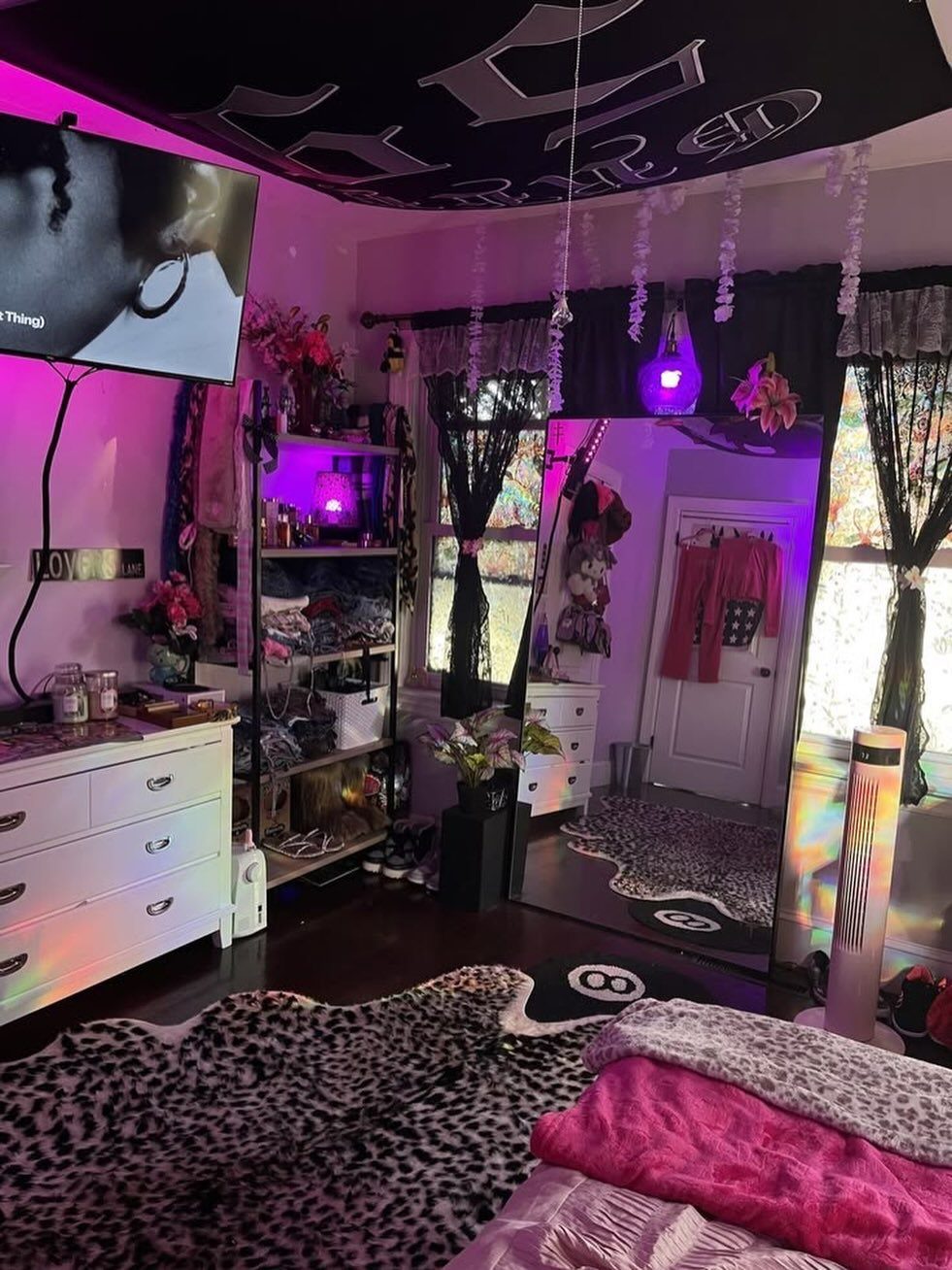 Bedroom with purple lighting, gothic ceiling canopy, leopard print rug, and black lace curtains.