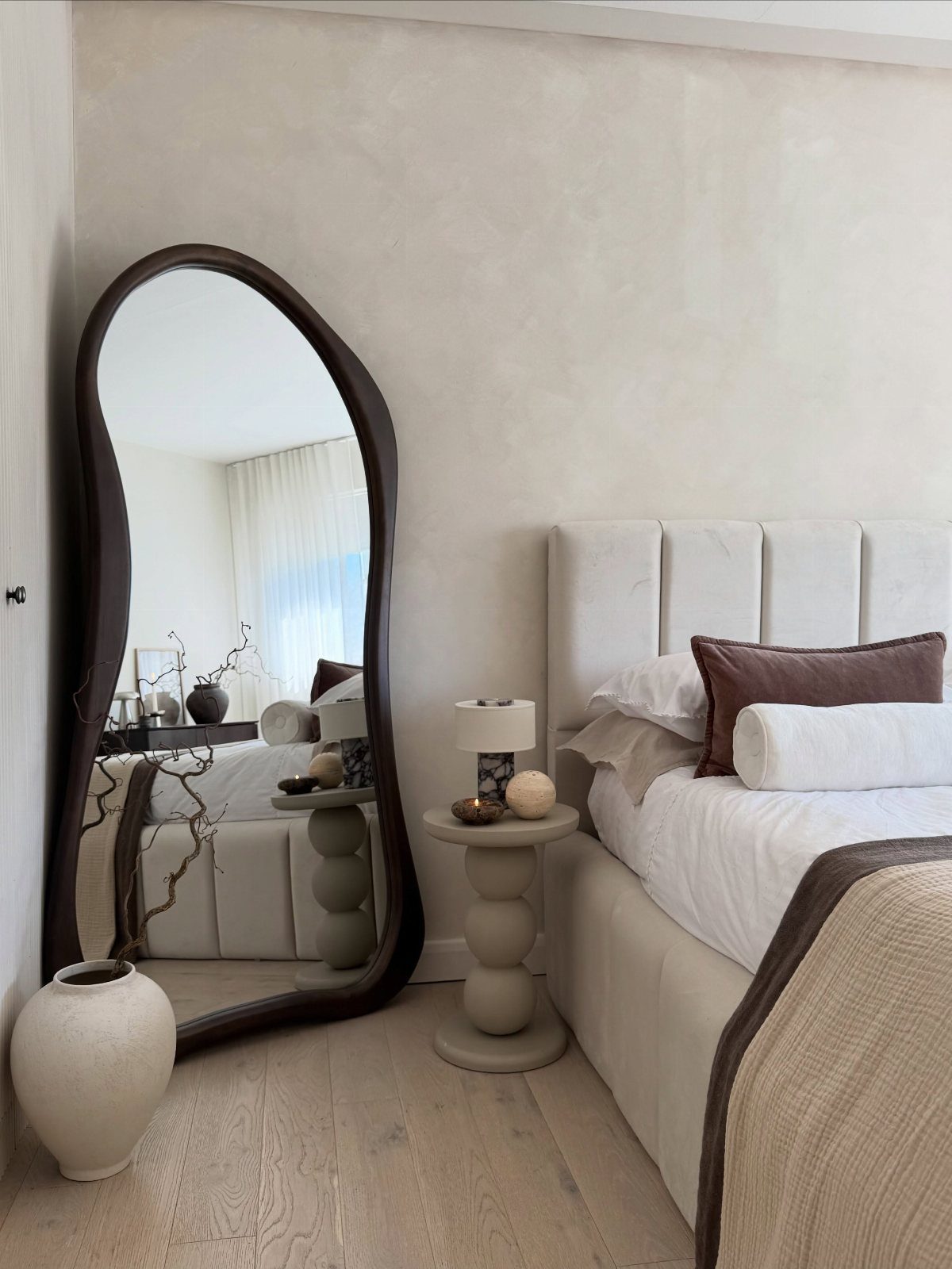 Large irregularly shaped full-length mirror leaning against a wall in a neutral bedroom