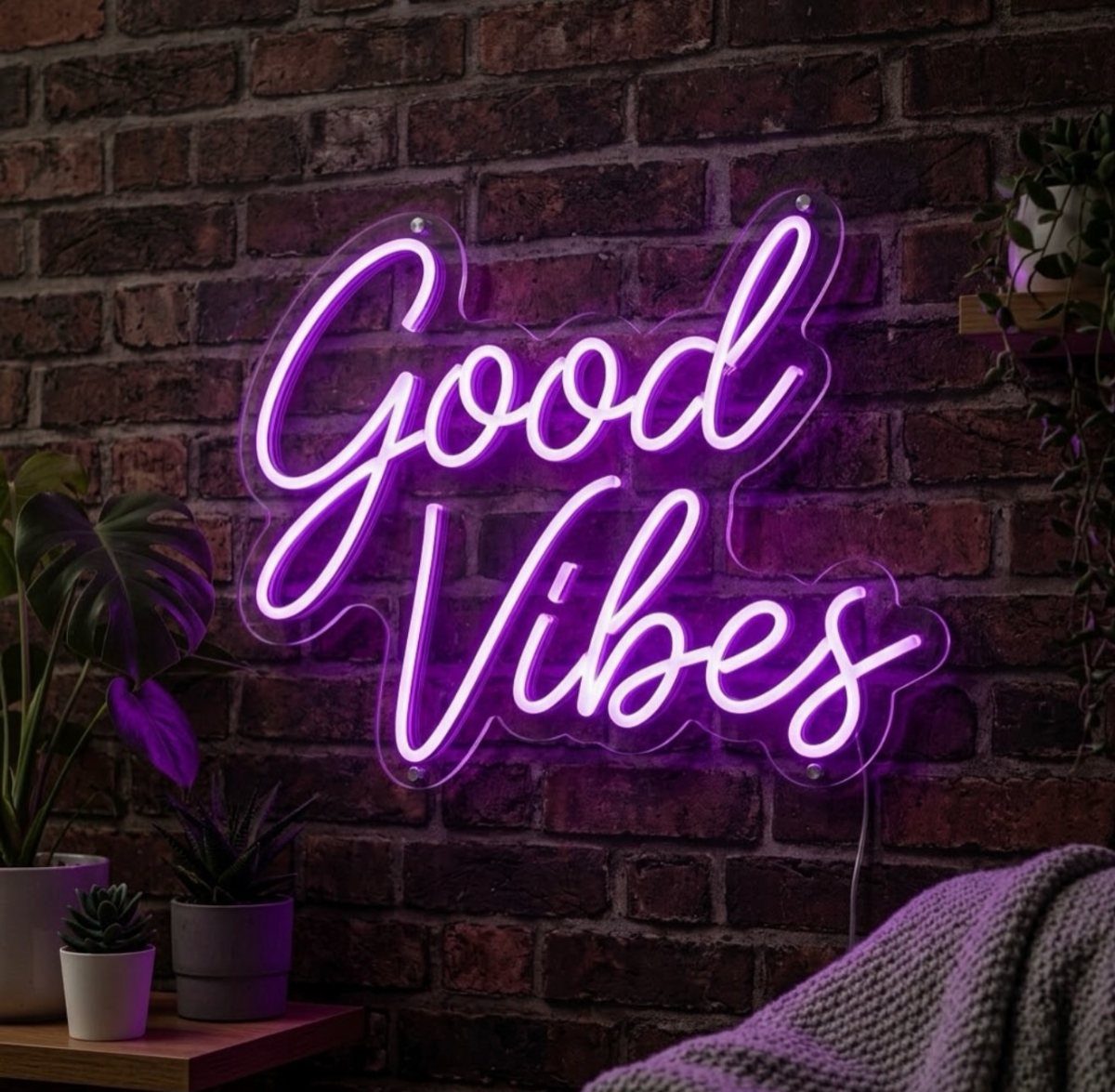 Purple neon Good Vibes sign on a brick wall with potted plants.