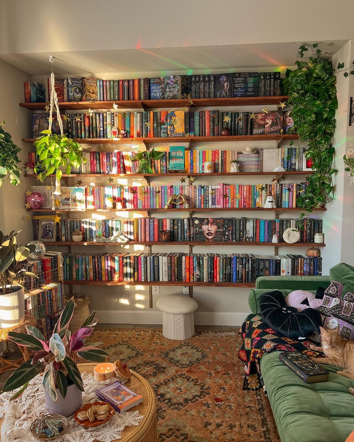 Cozy reading nook with wall-to-wall bookshelves, green velvet chaise, and indoor plants.
