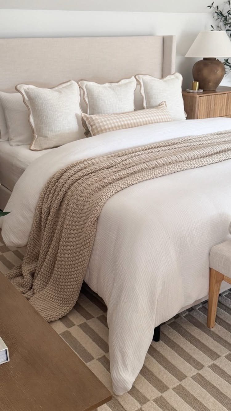 Beige chunky knit textured throw blanket draped over a white bed with pillows.