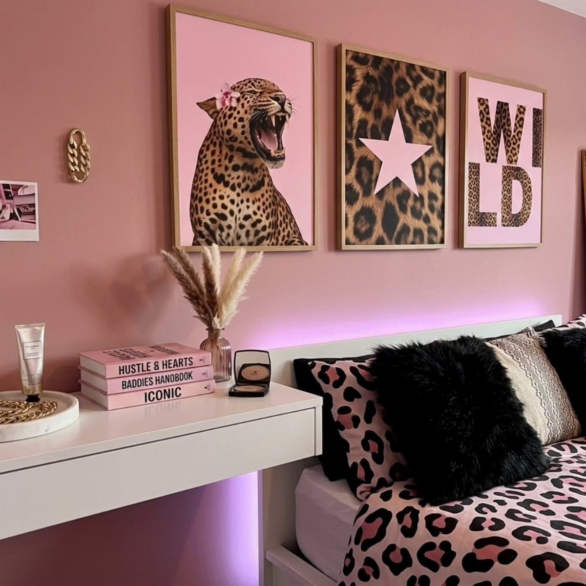 Three leopard themed framed prints on a pink wall above a white desk.