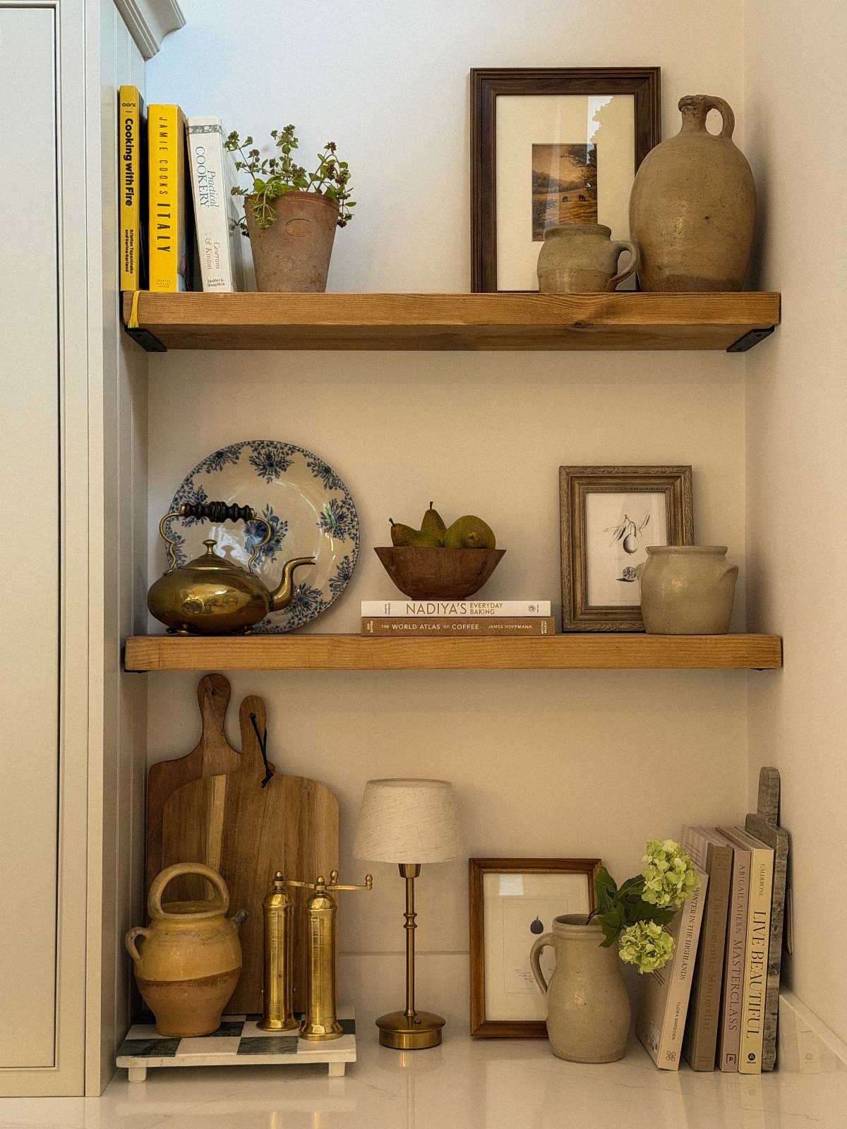 Wooden floating shelves styled with vintage ceramics, books, and framed art in a cozy room.