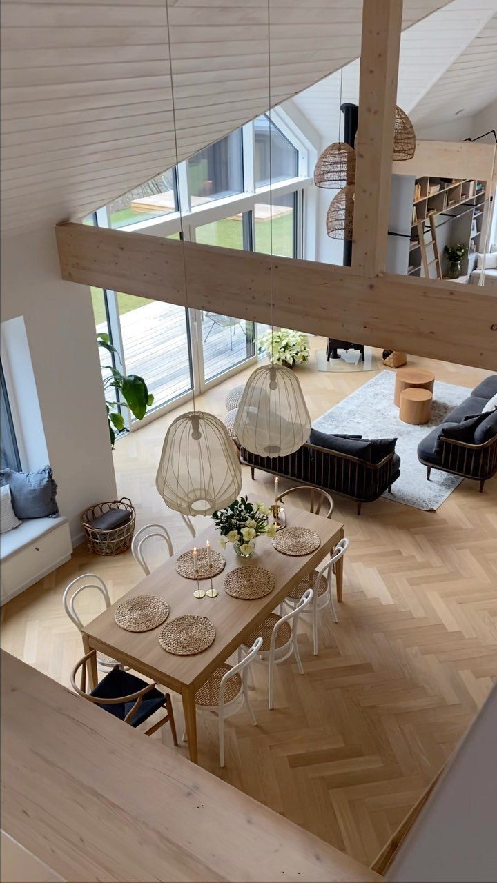 Bright open living space with light wood floors, white chairs, and woven pendant lamps.