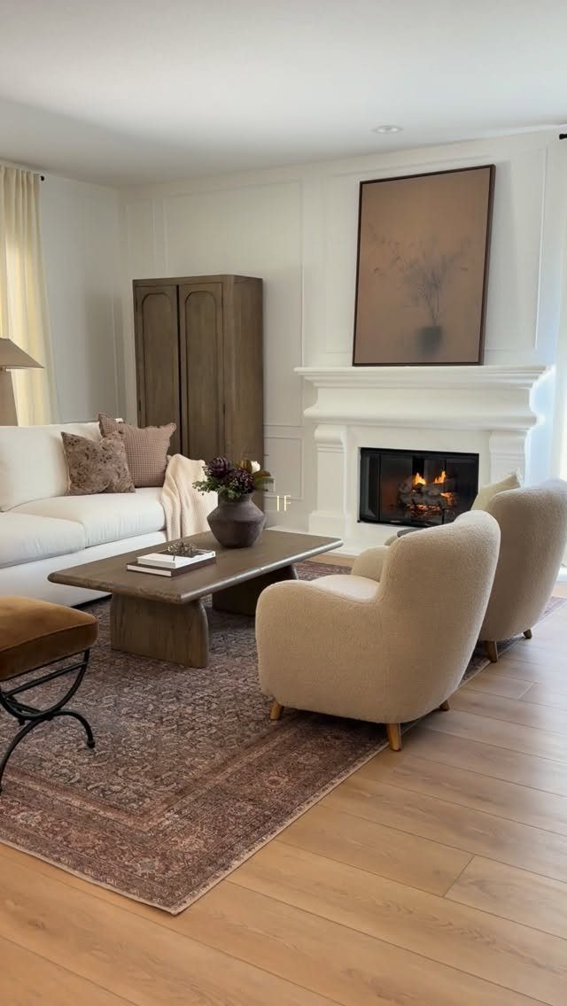 Living room with cream armchairs, white fireplace, and stone coffee table on patterned rug.