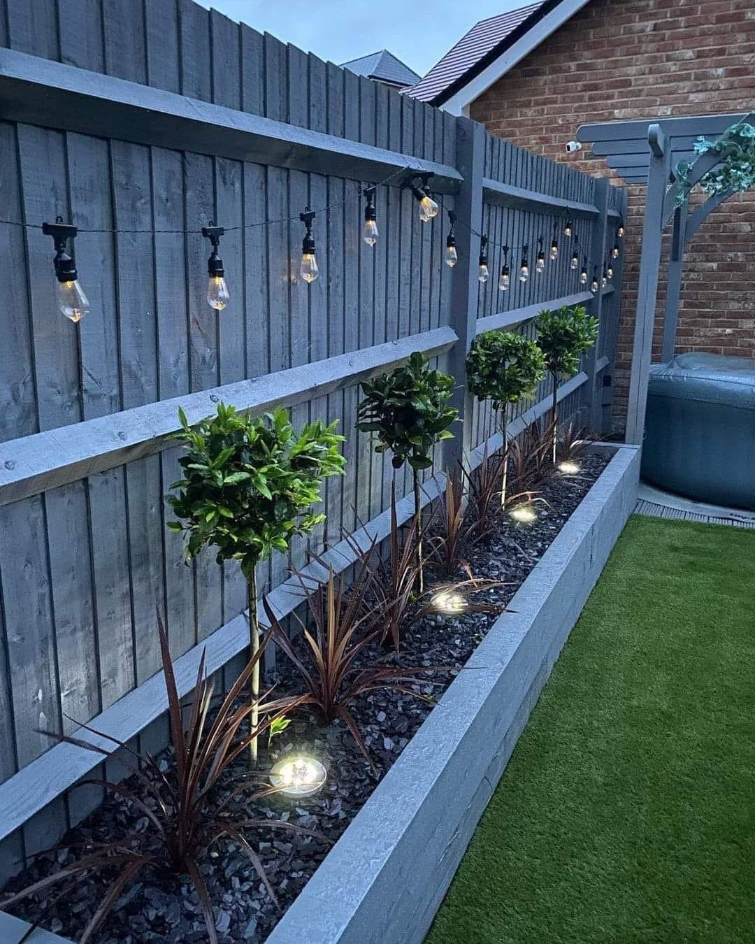 Garden bed with dark gravel and small trees illuminated by ground lights