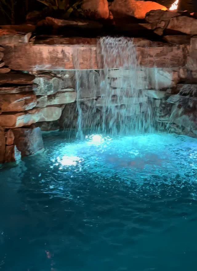 Underwater blue lighting illuminating a rock waterfall feature in a swimming pool