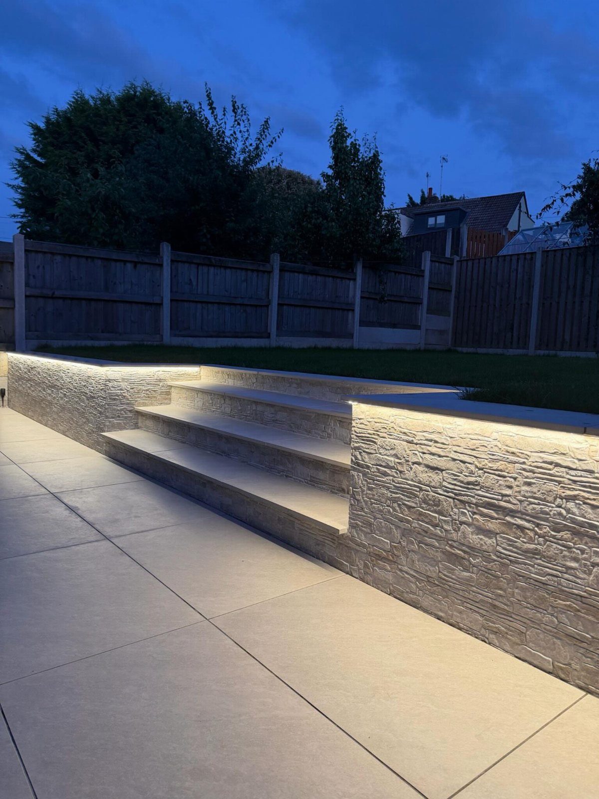 Textured stone wall and steps in a backyard illuminated by warm linear lighting