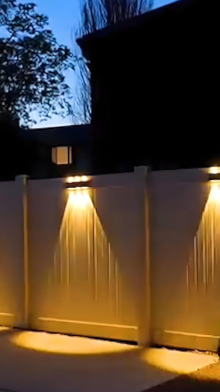 Warm yellow lights mounted on a white vinyl fence casting downward glows.