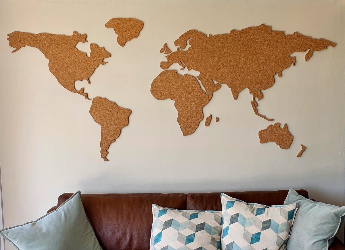 Cork world map mounted on a white wall above a brown leather sofa.