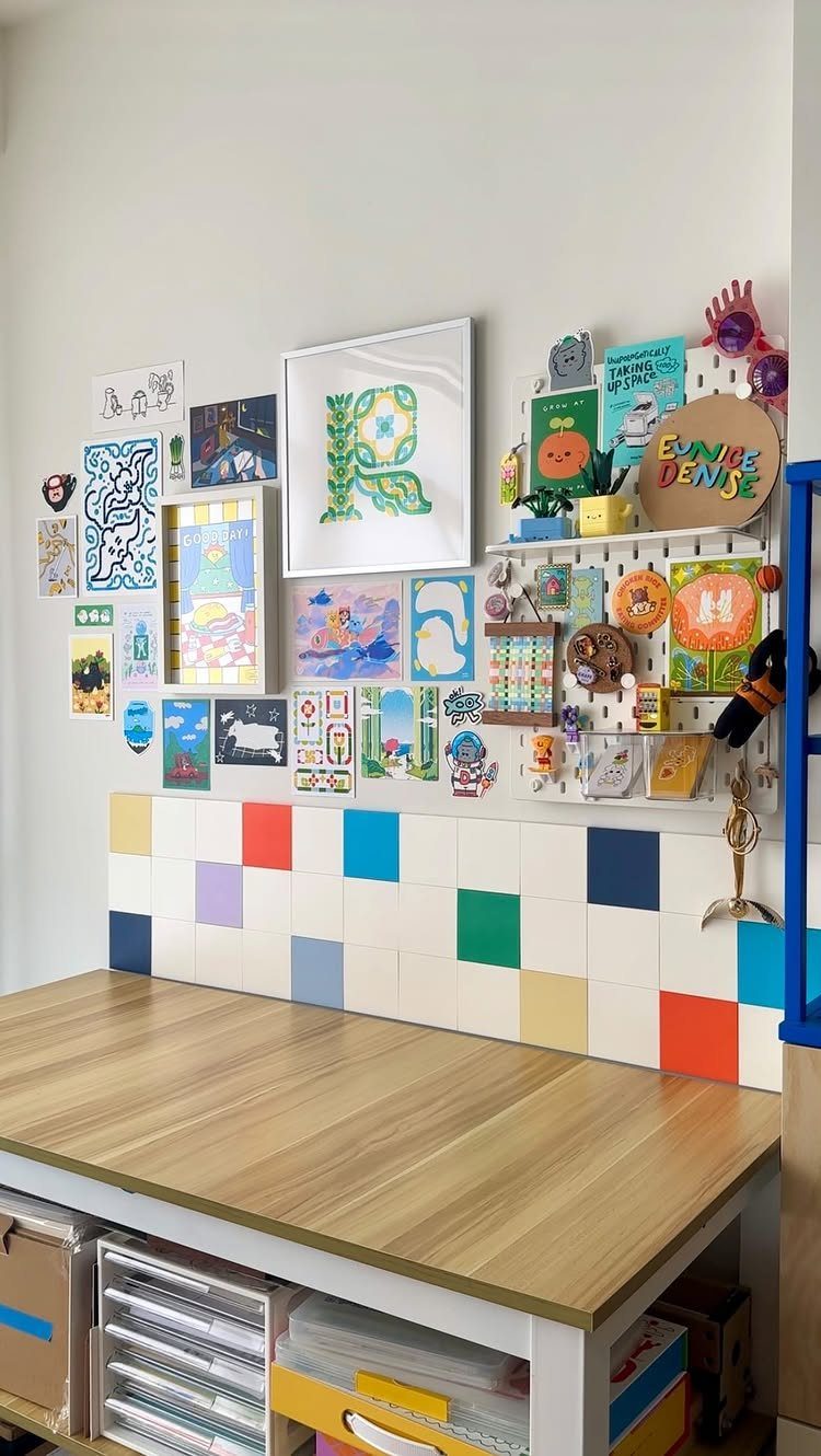 Craft room workspace with a wooden desk and art-covered white wall.