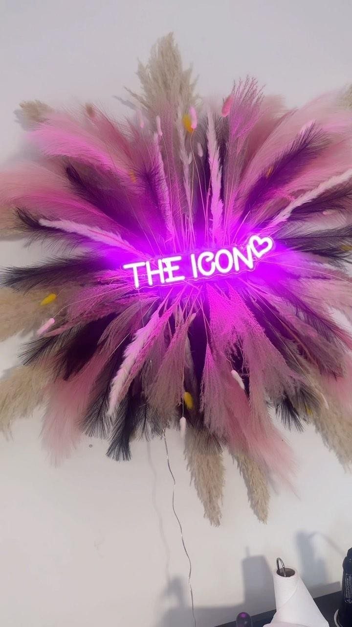 Pink neon sign reading THE ICON centered in a fluffy pampas grass arrangement.