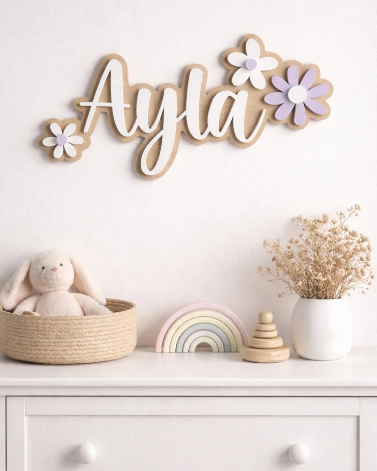 Wooden name sign Ayla with flowers on a wall above a white dresser.