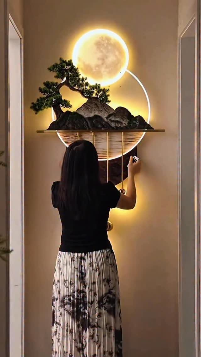 DIY LED Light Lamp Ideas: 27 Backlights, Pendants, Table Lamps 15 Woman adjusting a wall-mounted LED lamp with a glowing moon and bonsai tree.