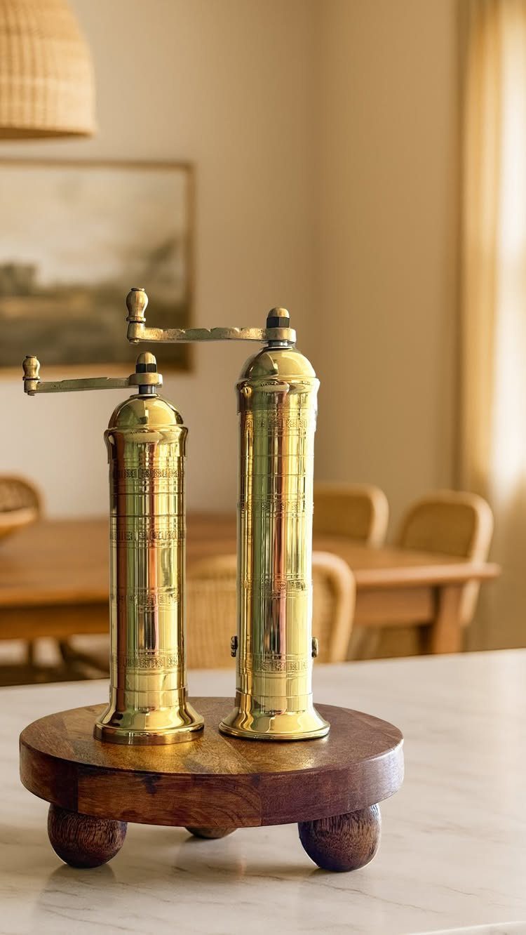 Brass salt and pepper mills on a round wooden tray on a marble counter.