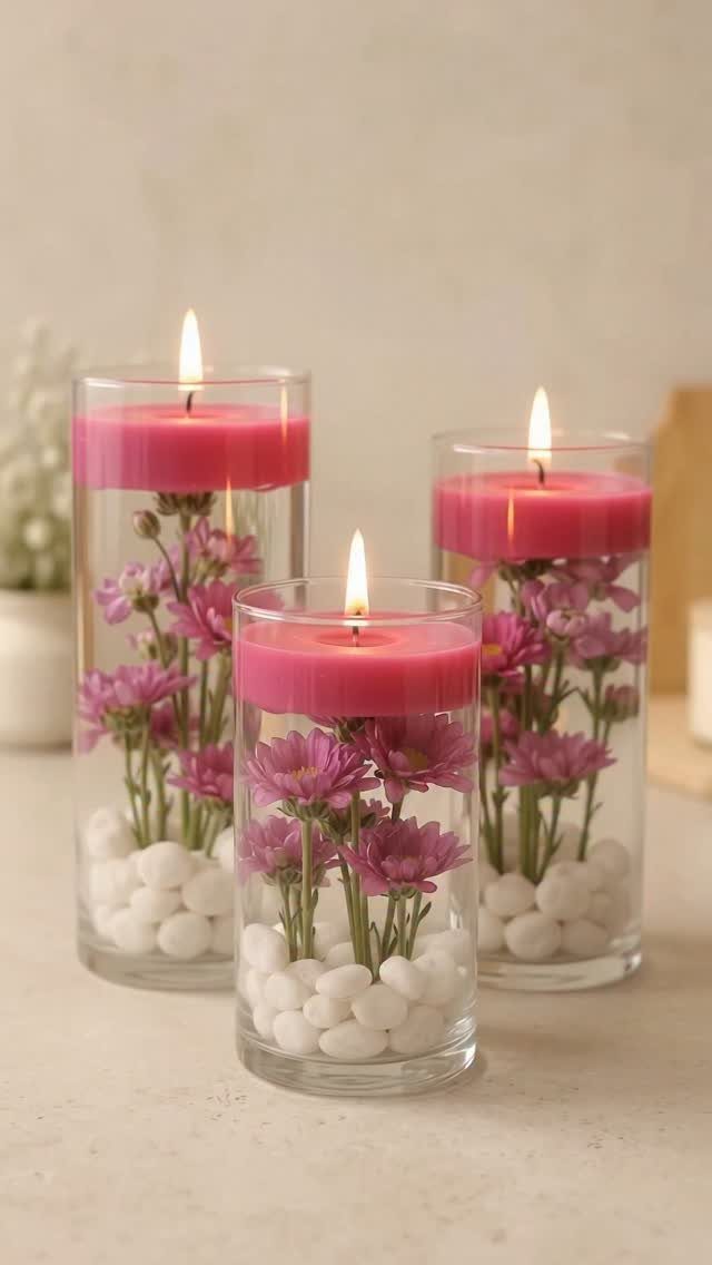 Three glass vases with white pebbles, pink flowers, and floating lit pink candles.