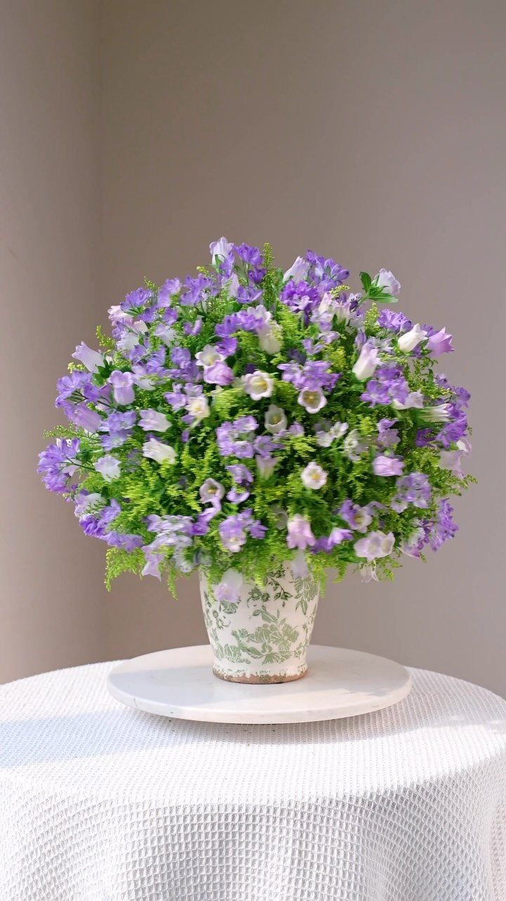 Purple flowers in a floral ceramic vase on a white pedestal and table.
