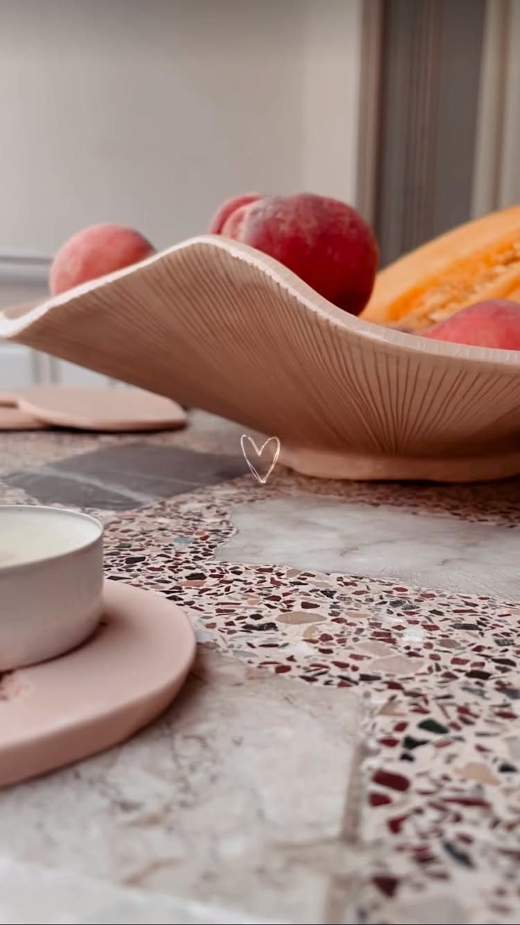 Wooden bowl filled with red peaches and melon on a terrazzo countertop.
