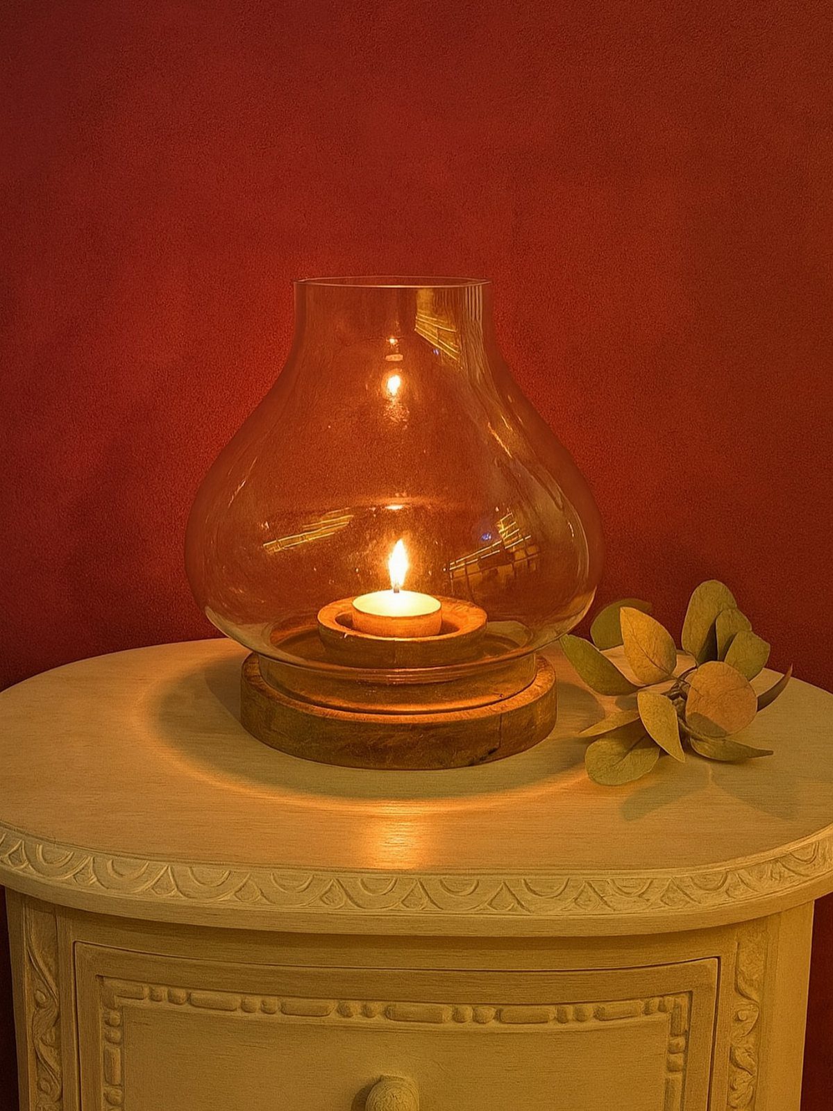 Lit tea light candle inside a glass hurricane vase on a white table.