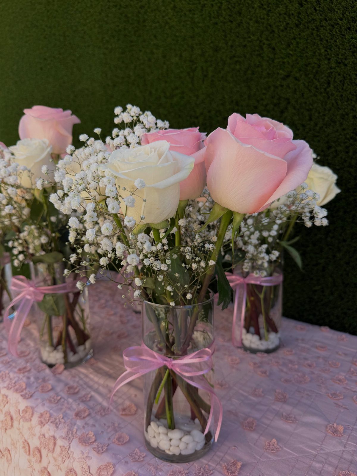 Pink and white roses with baby's breath in small glass vases with pink ribbons.