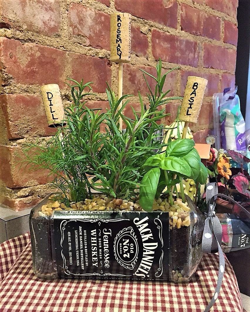 Herbs planted in a horizontal whiskey bottle planter on a checkered tablecloth.