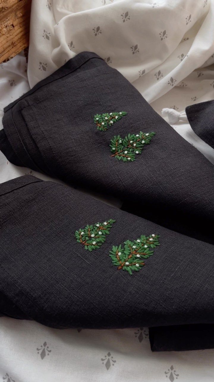 Black kitchen towels with green and white floral embroidery on white patterned fabric