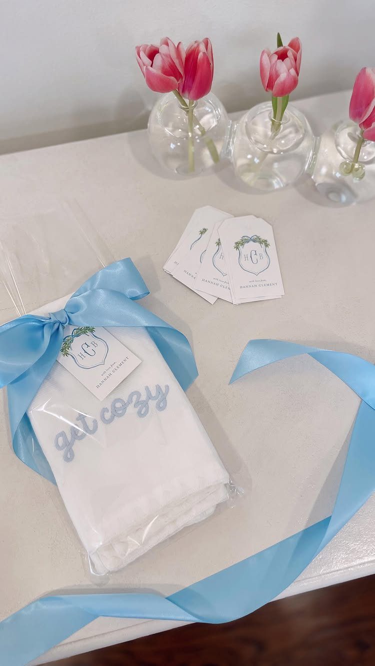 White embroidered towel wrapped in plastic with a blue ribbon and pink tulips.