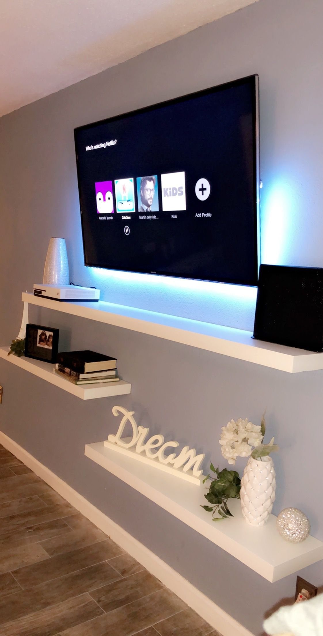 Floating Shelf Under TV Ideas: 31 Styles for Living Rooms 2 Wall-mounted TV with blue backlighting and two white floating shelves below it.