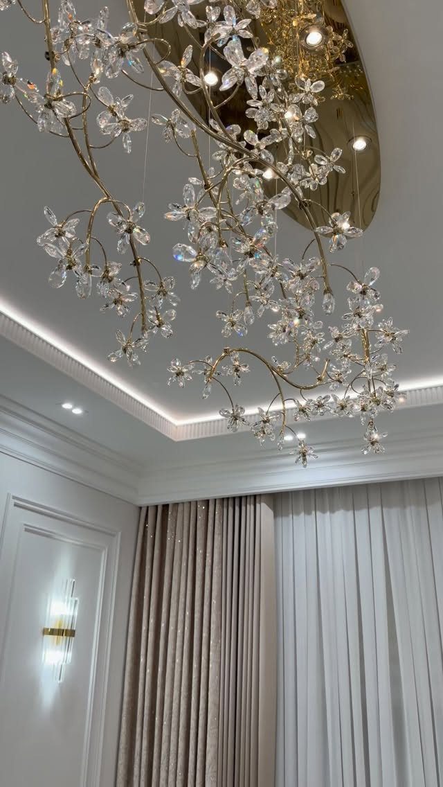 Ornate crystal chandelier with floral glass details hanging from a gold reflective ceiling