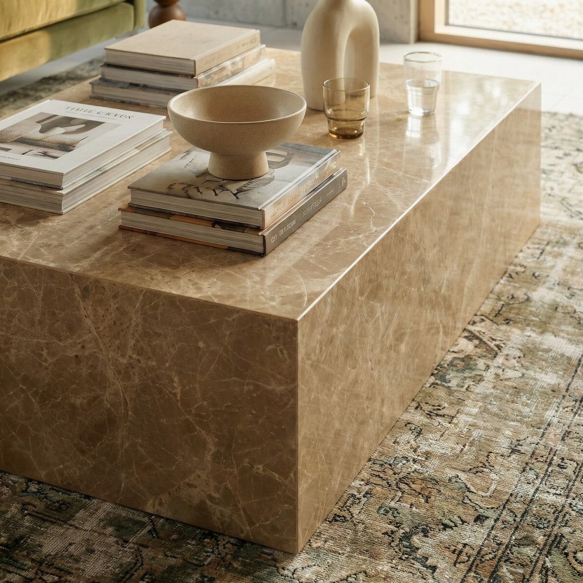 Brown marble coffee table with books and decor on a patterned rug.