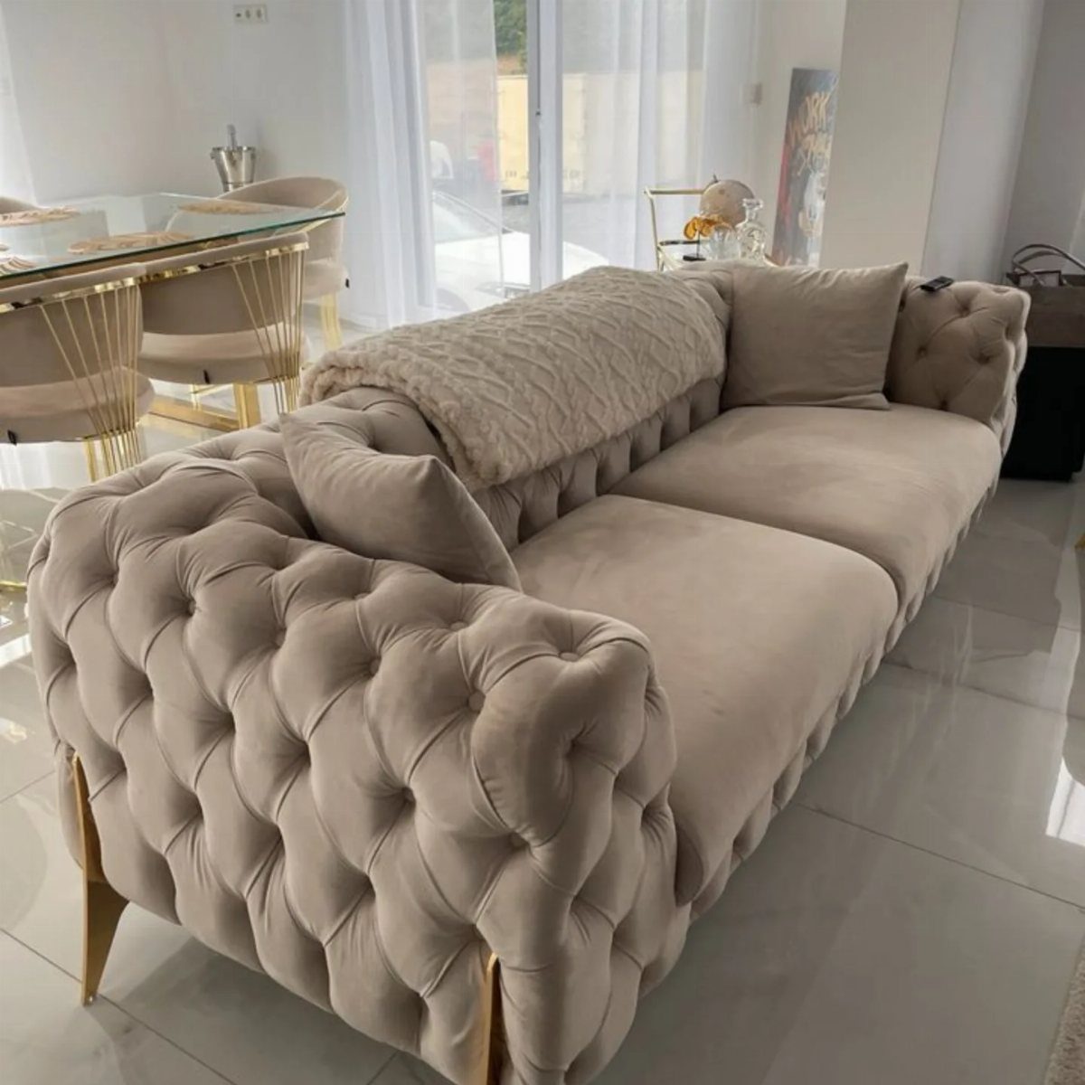 Beige velvet tufted sofa with gold legs in a bright, modern living room