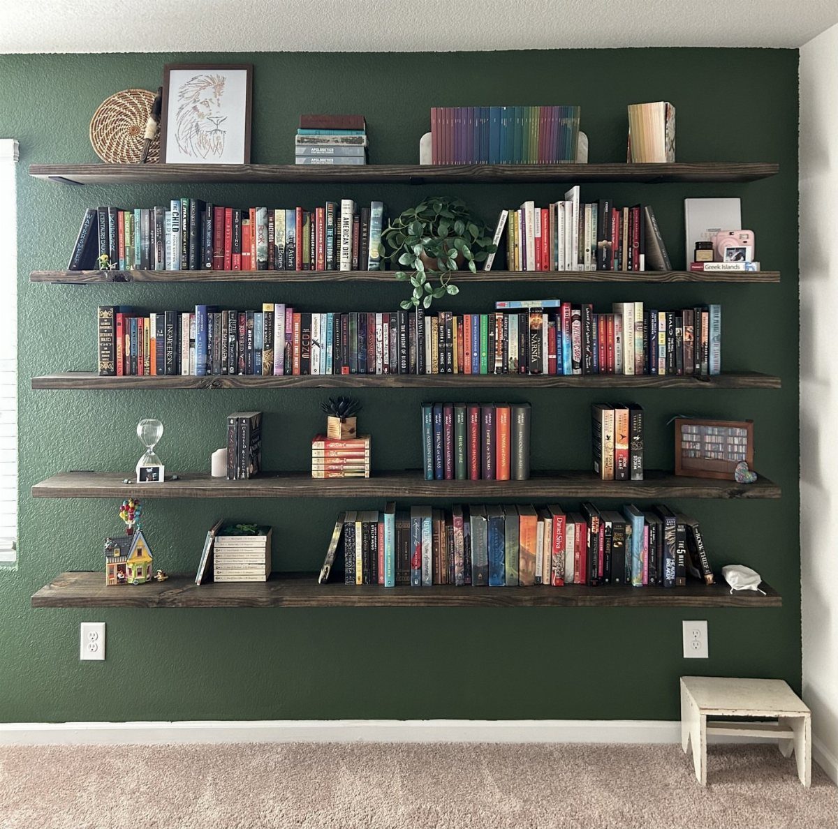 Dark wood floating shelves filled with books on a deep green wall.