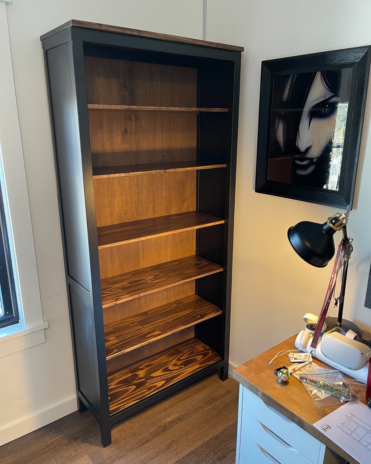 Black bookshelf with wood shelves standing next to a white wooden desk.