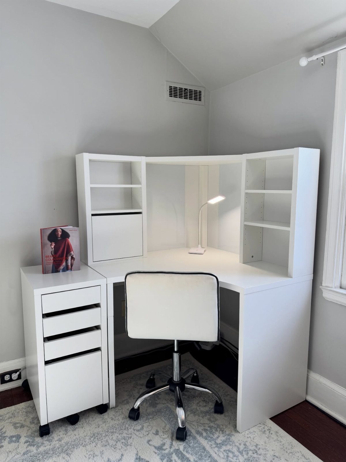 White L-shaped corner desk with built-in shelving and a matching white office chair.