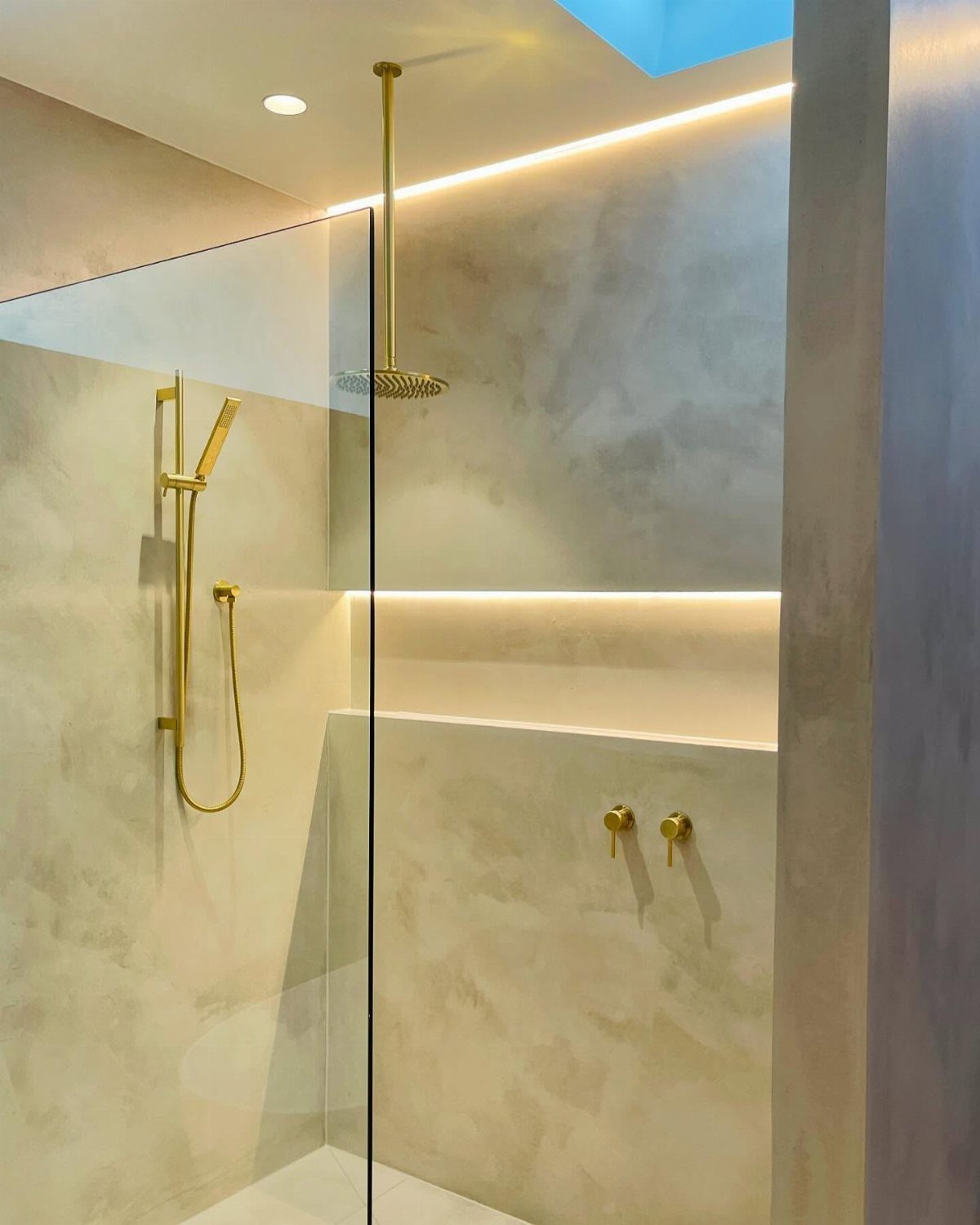 Modern shower with gold fixtures and warm indirect cove lighting in the ceiling.