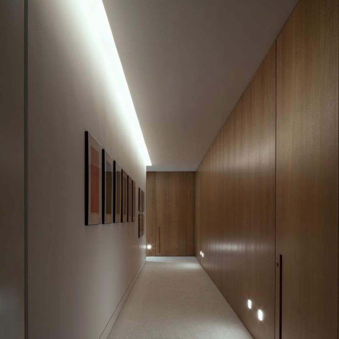 Hallway with indirect cove lighting illuminating a series of framed artworks on a wall.
