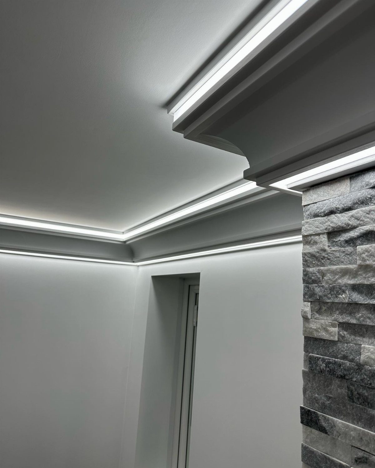 White crown moulding with integrated cove lighting illuminating a modern white ceiling.