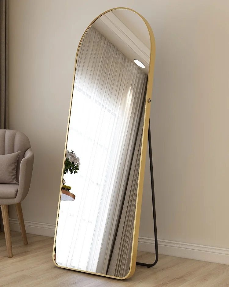 Large oval floor mirror with gold frame and black stand in a bright room.