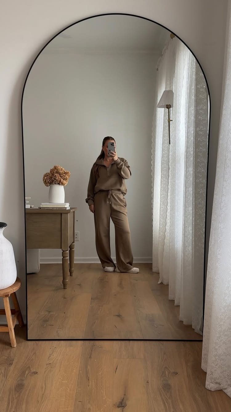 Arched floor mirror with black frame reflecting a woman in a bright room.