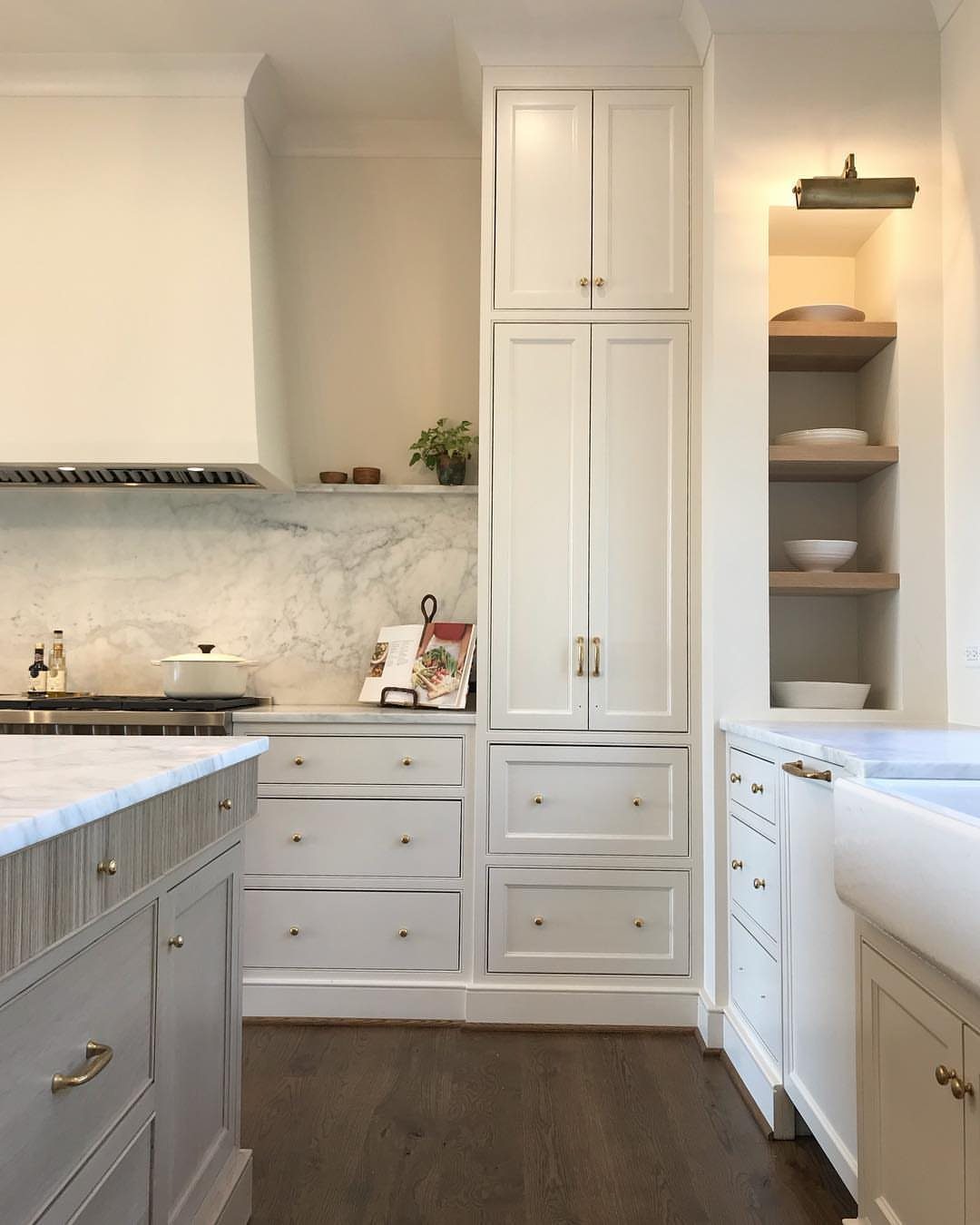 Wooden open shelves recessed in a wall above a white farmhouse kitchen sink.