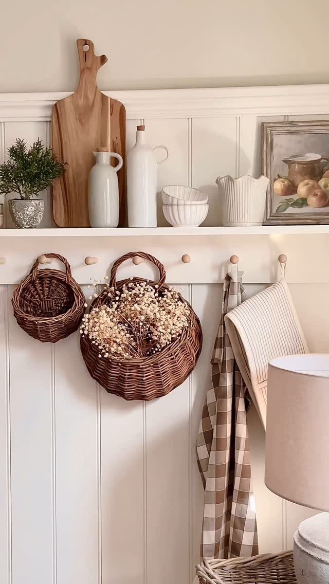 Woven brown baskets hanging from pegs below a white kitchen shelf with ceramics.