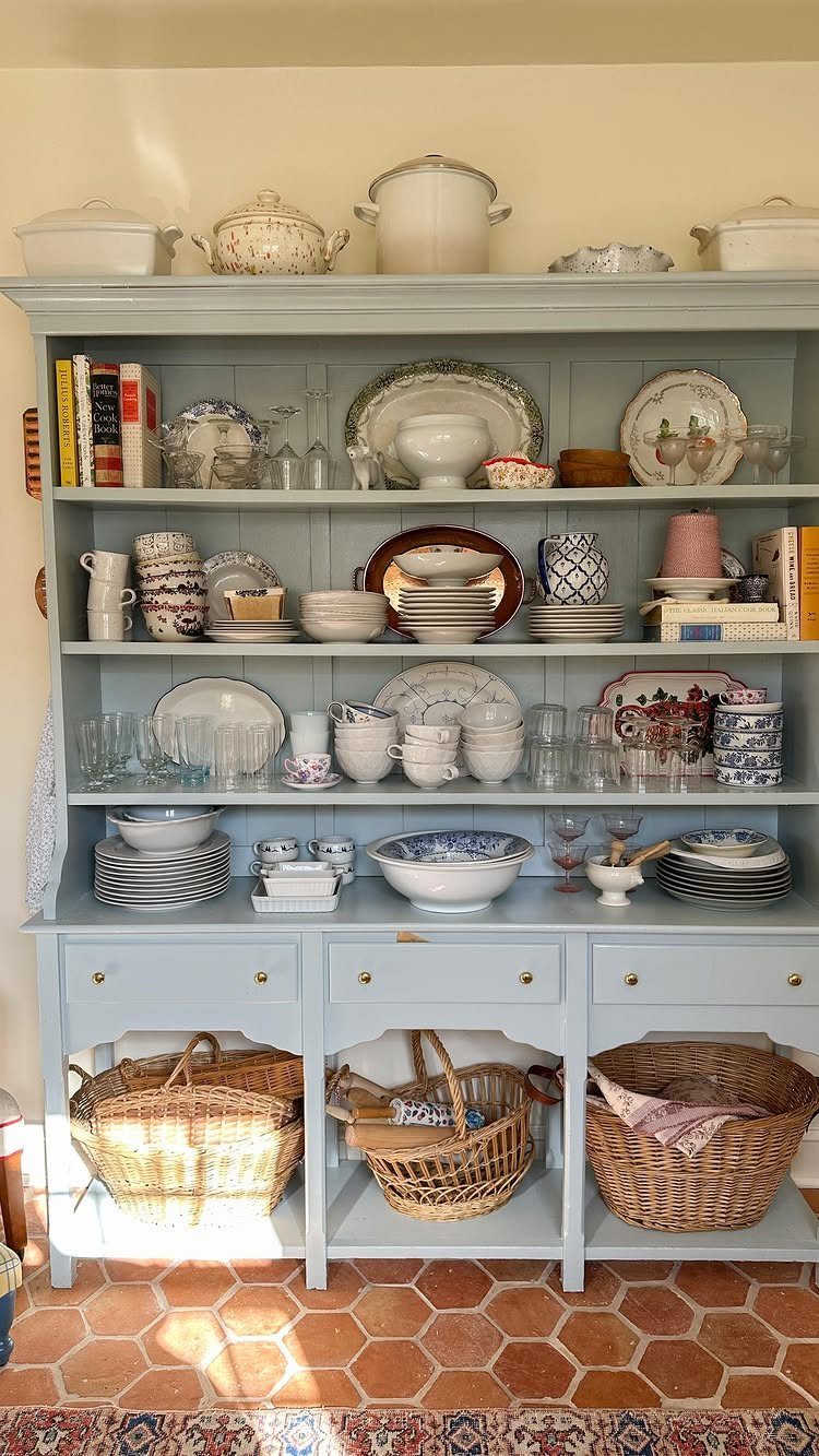 Light blue open shelving hutch filled with ceramic dishes and woven baskets.