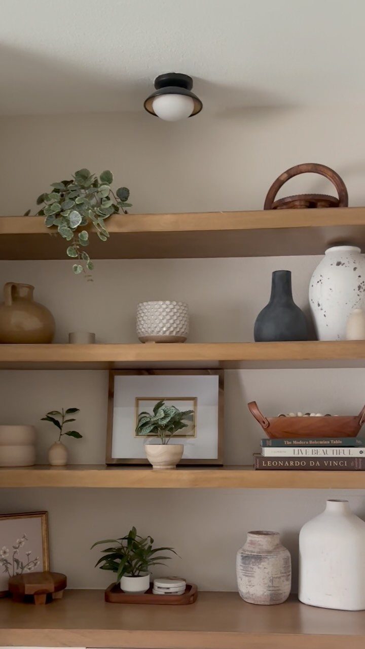 Wooden open shelves decorated with small green plants, ceramic vases, and framed art.