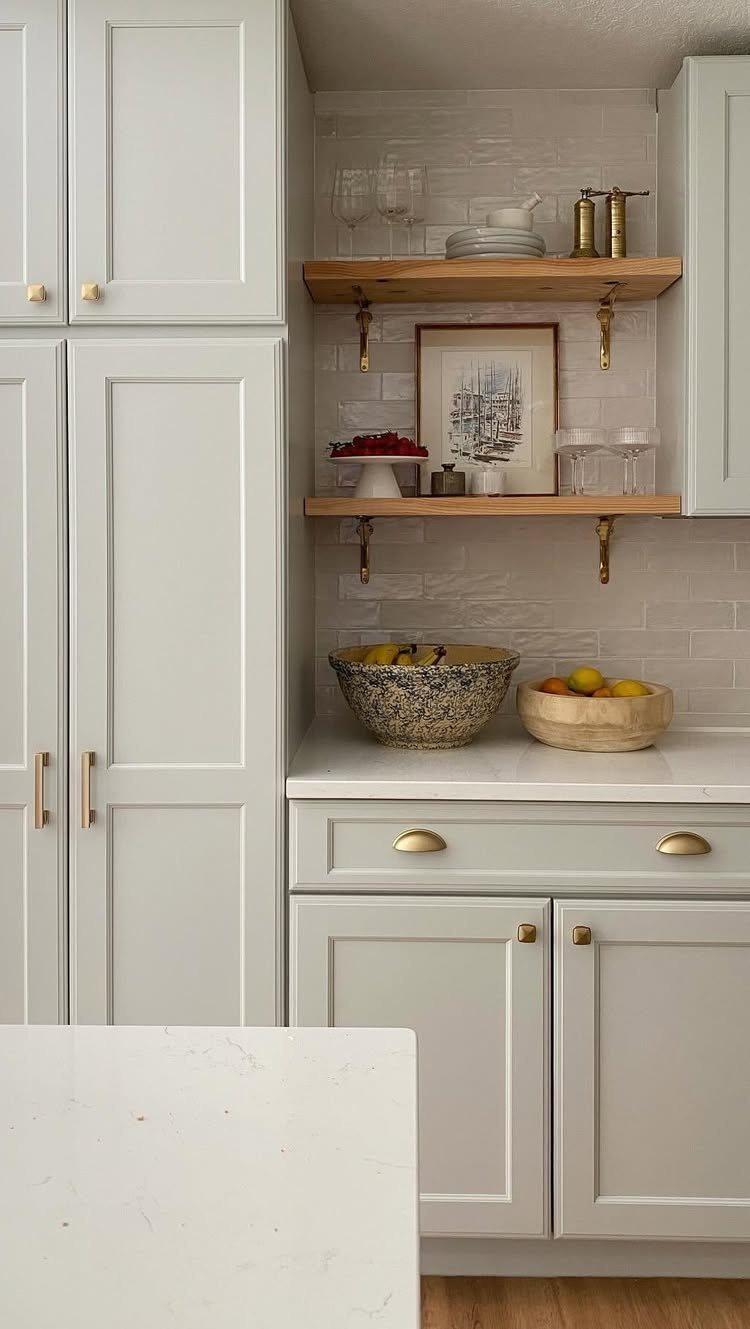 Wooden open shelves with gold brackets in a light grey kitchen with white tiles