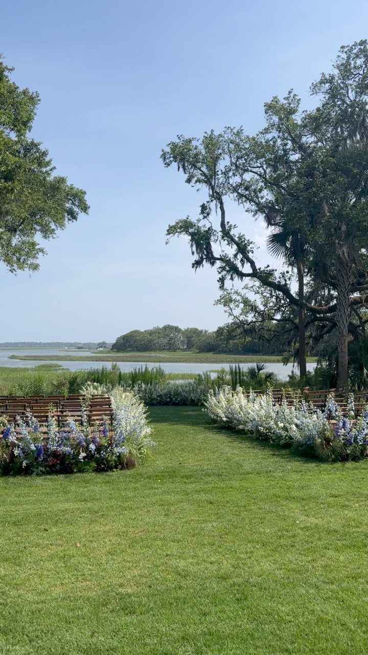 Outdoor wedding ceremony aisle lined with colorful flowers and wooden benches by a lake.