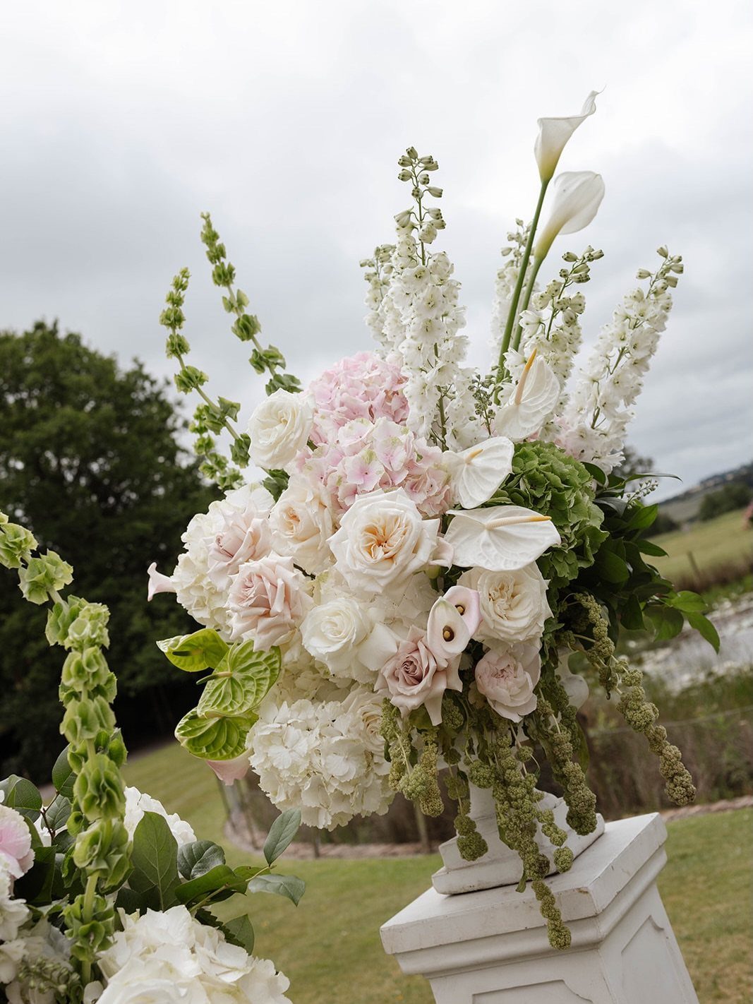 White and pink floral arrangement in a white stone urn on a pedestal.