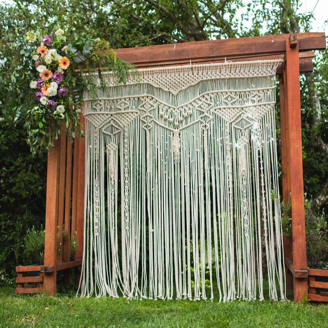 Cream macramé backdrop hanging from a wooden arbour with colorful flowers in a garden